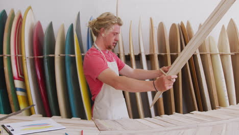 fabricante de tablas de surf masculino caucásico trabajando en su estudio y haciendo una tabla de surf de madera