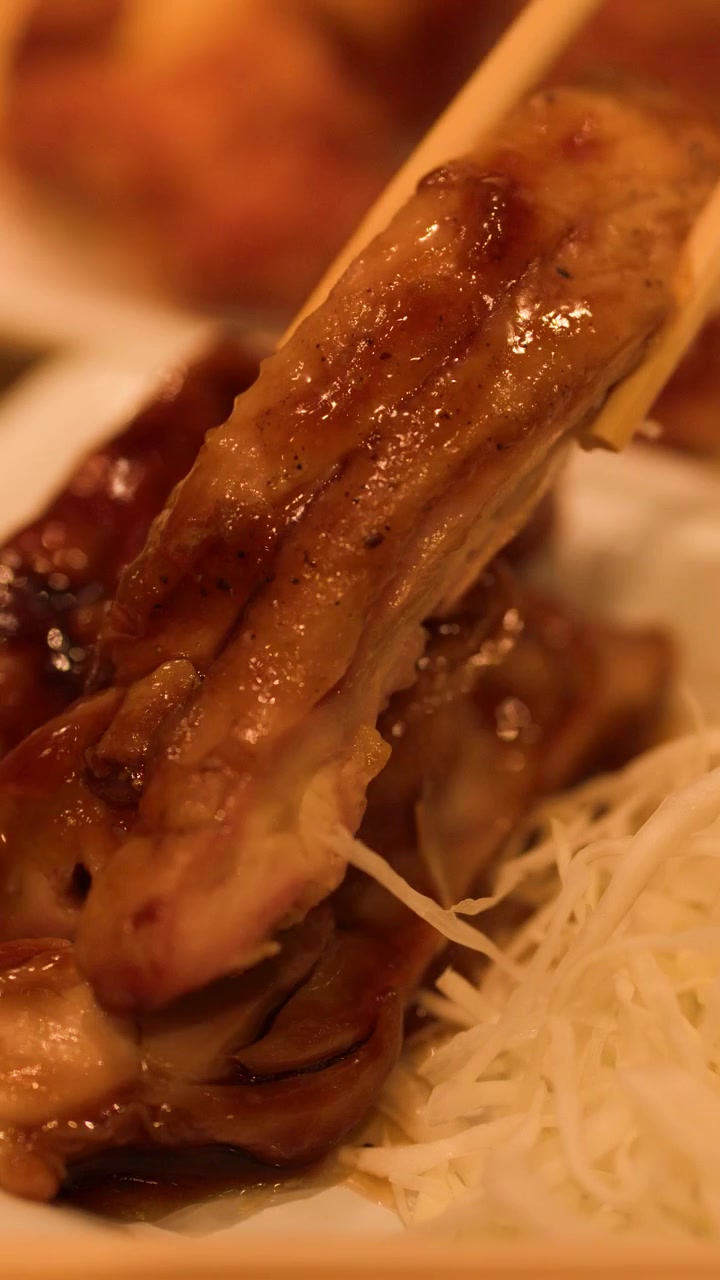 Hashis de madeira levantam um pedaço de frango teriyaki glaceado de um prato com repolho desfiado