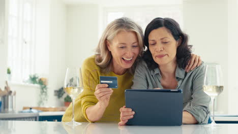 Same-Sex-Mature-Female-Couple-With-Credit-Card-Using-Digital-Tablet-At-Home-To-Book-Holiday-Or-Shop