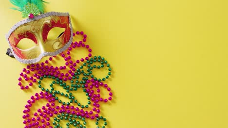 video of masquerade mask, mardi gras beads and feathers on yellow background with copy space