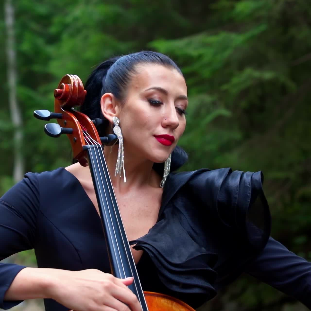 Luxury woman plays the cello. Beautiful girl violinist playing violin on summer landscape. Attractive woman in black dress enjoying musical art while playing instrument.