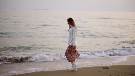 girl in elegant clothes walks along the seashore view from the side