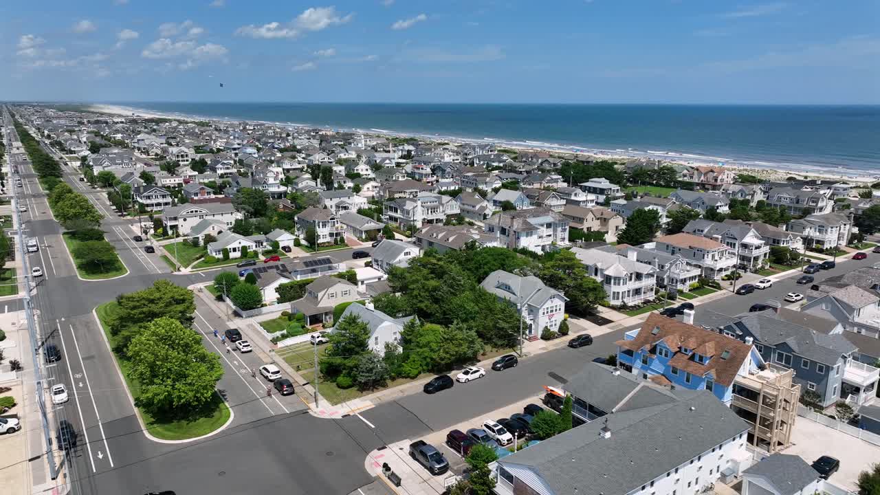 Noble beach houses with porch and grey roof near stone harbor beach. Sunny summer day In New Jersey. Resting people at Sandy beach. Aerial forward wide shot. Luxury properties and villas