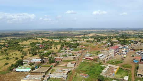 Aerial-view-overlooking-a-village-and-sunny-Amboseli-national-park,-in-Kenya---rising,-pan,-drone-shot