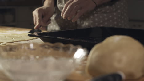 Hands-gently-scoop-cookie-dough-with-knife-into-baking-tray-in-kitchen