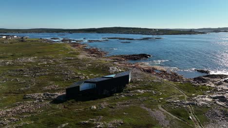 long studio modern architecture overlooking atlantic views with glistening sunlight on fogo island from an aerial orbital drone shot, newfoundland, canada