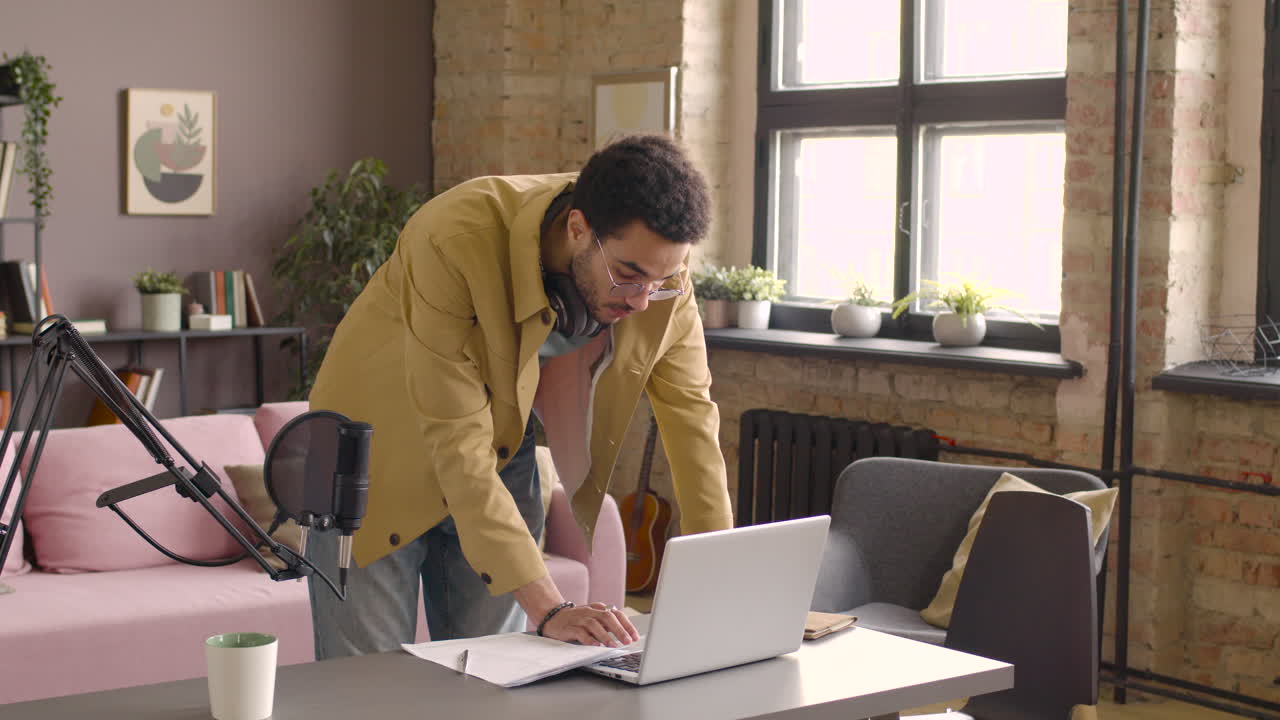 hombre con auriculares de pie usando una computadora portátil en el escritorio en una habitación con micrófono