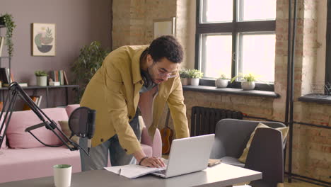 Man-With-Headphones-Standing-Using-On-Laptop-At-Desk-In-A-Room-With-Microphone