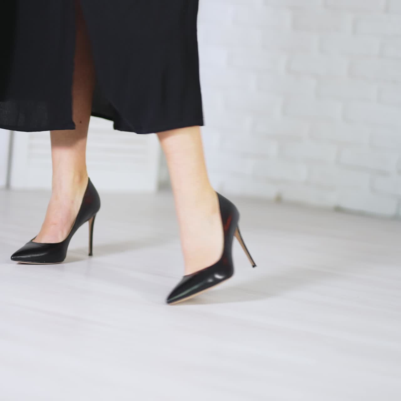 Elegant classic black shoes demonstration. Woman in long black skirt showing the high-heeled stiletto footwear. White backdrop