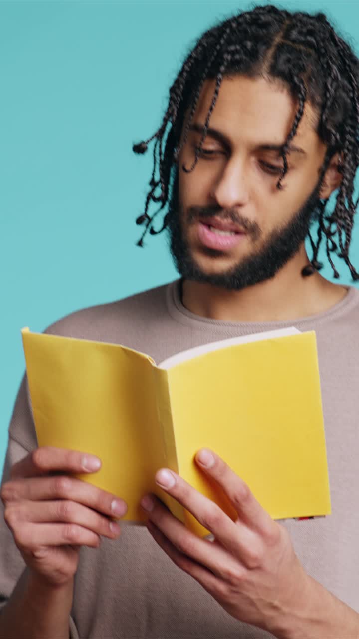 Vidéo verticale : homme lisant un livre à couverture rigide nouvellement publié par une maison d’édition, arrière-plan de studio
