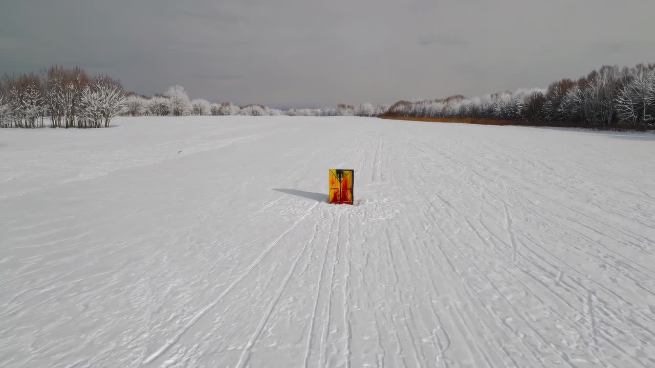 Colorful signal marking a large snowy field, featuring tire tracks and surrounded by barren, leafless trees. Capturing the serene beauty of winter's tranquil landscape