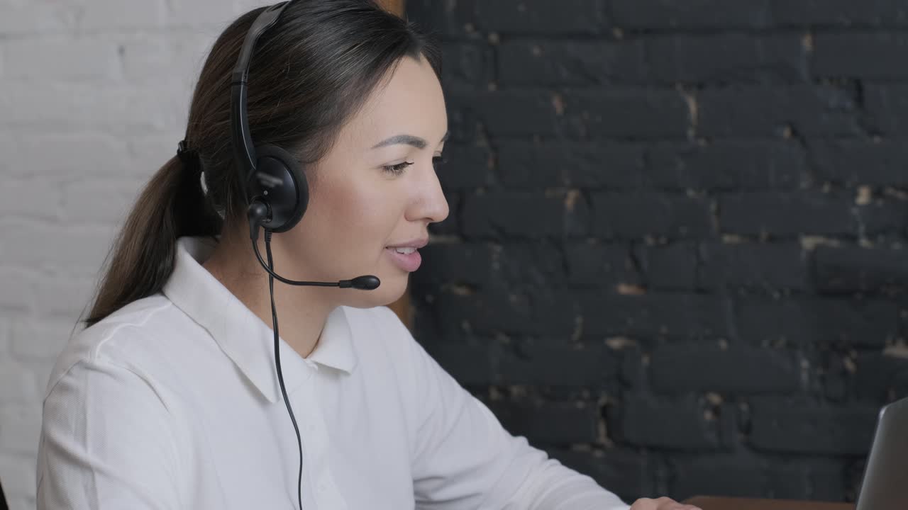 Smiling woman call centre operator, customer support agent wears headset consults client online typing on laptop, talk in internet computer chat, helpline operator secretary make conference video call