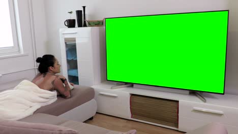 woman lying on sofa and watching green screen television