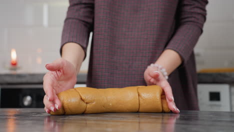 lower body view of woman adjusting brown dough on kitchen counter, in warm modern kitchen setting with blurred background featuring red candle and kitchen appliances