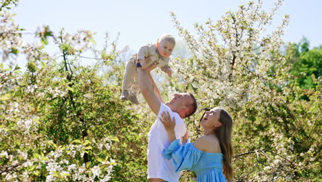 parents amuse their little baby tossing him up. caucasian family having fun outdoors together in spring garden.