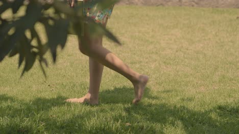 woman in shorts walking barefoot on grass with green book in hand, slow motion panning shot in the summer garden