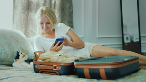 A-Woman-Going-On-Vacation-Uses-A-Smartphone-Around-A-Half-Packed-Travel-Bag