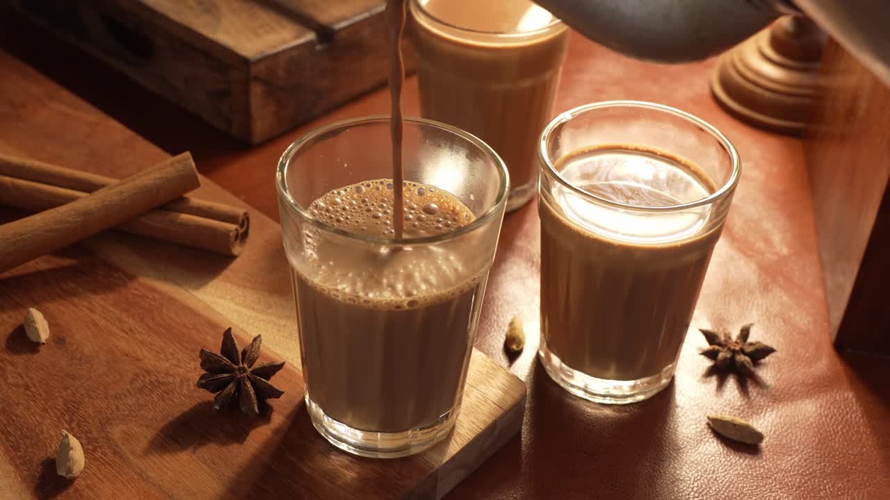 Chai indiano servito in tazze di vetro, preparato in un bollitore di metallo con masalas aromatici. Viene versato nel vetro.