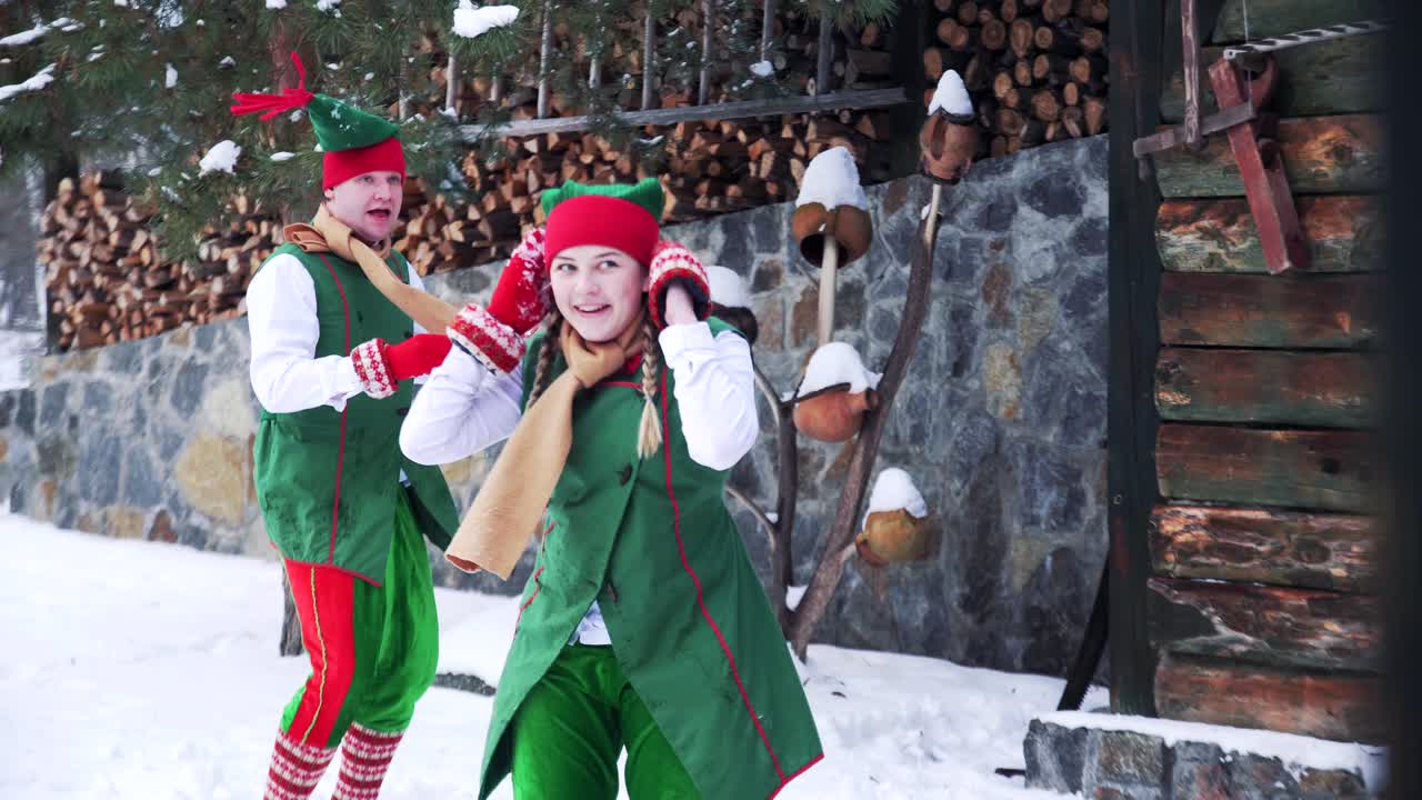 Joyful elves playing in the snow near the house. Fairy heroes elves a boy and a girl having snowball fight on winter holidays