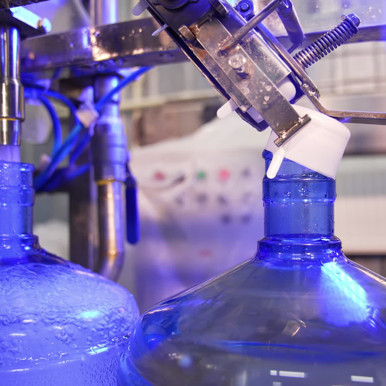 Water is poured into big blue bottle and overflows it. Filled bottles are covered with plastic white corks. Close up