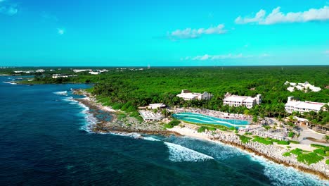 Vista-Aérea-De-Tulum-México-Volando-Sobre-El-Mar-Caribe-Y-Hacia-La-Piscina-Infinita-De-Un-Resort-De-Lujo