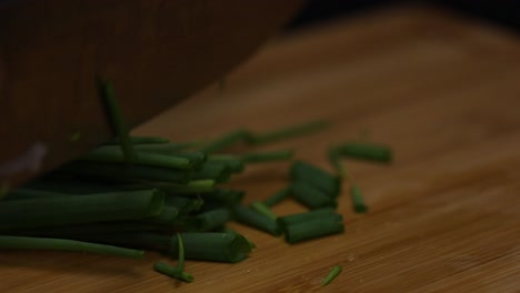 Close-up-shot-as-chopping,-slicing-the-green-of-a-spring-onion-on-a-wooden-desk-with-a-sharp-knife