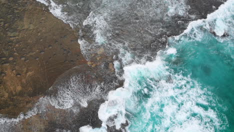 a sweeping aerial top view of waves crashing against a rock face on a tropical island