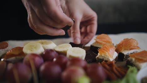 las manos de las mujeres ponen pedazos de chocolate en una bandeja de madera con comida decorándola.