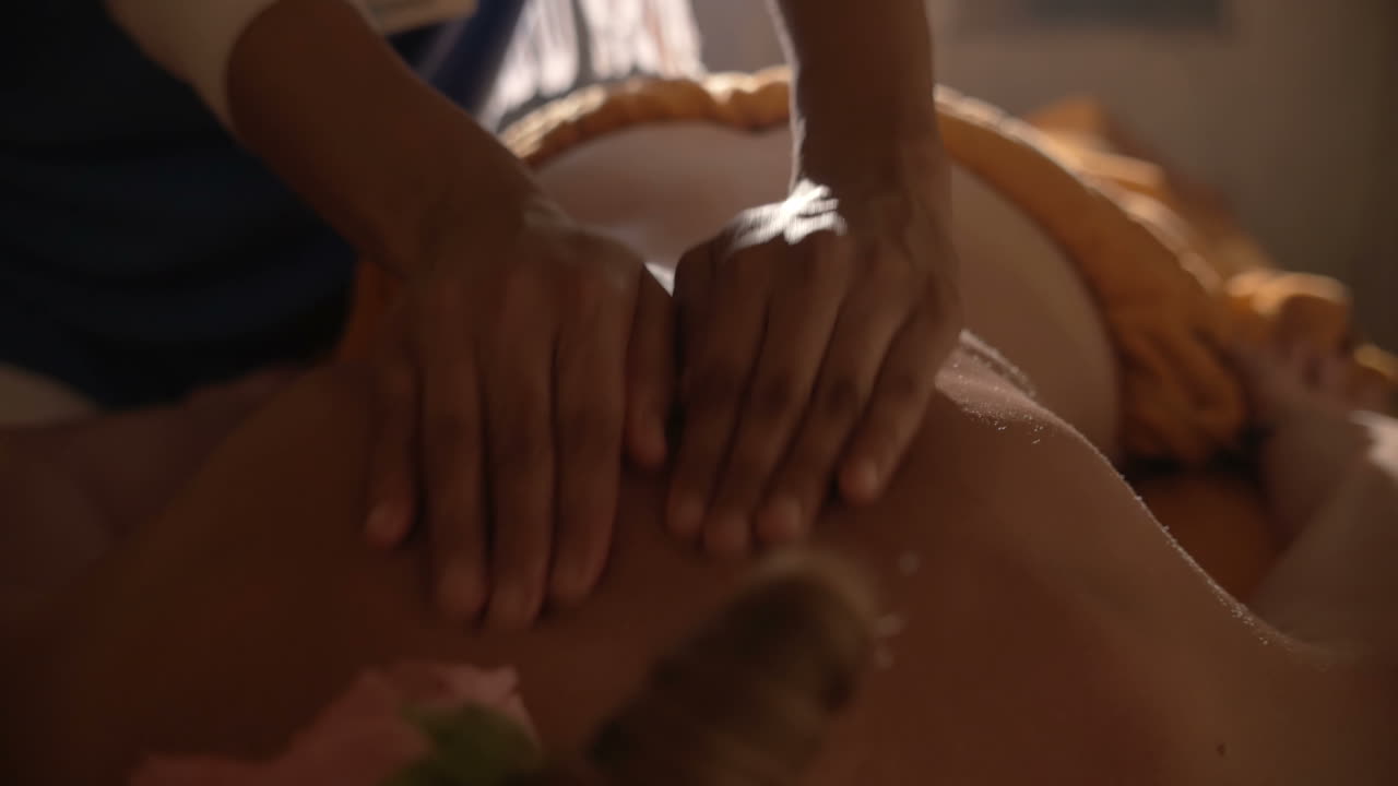 mujer joven recibiendo masaje corporal de piedra caliente en el spa