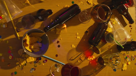 overhead shot of messy table covered with empty wine glasses with beer bottles and snacks after house party