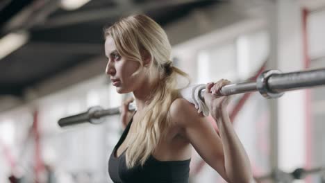 pretty sportswoman squatting with barbell at bodybuilding training in gym.