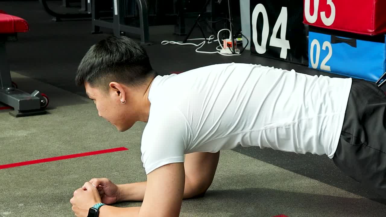 屋内で、決意に満ちた男性アスリートが体幹を強化する前腕プランクエクササイズを行う横からの視点。