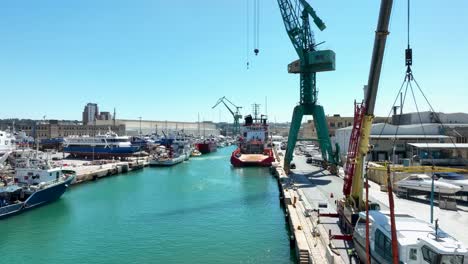 Aerial-drone-shot-flying-low-to-high-over-blue-sea-near-several-boats-and-ships-in-a-very-busy-boat-yard