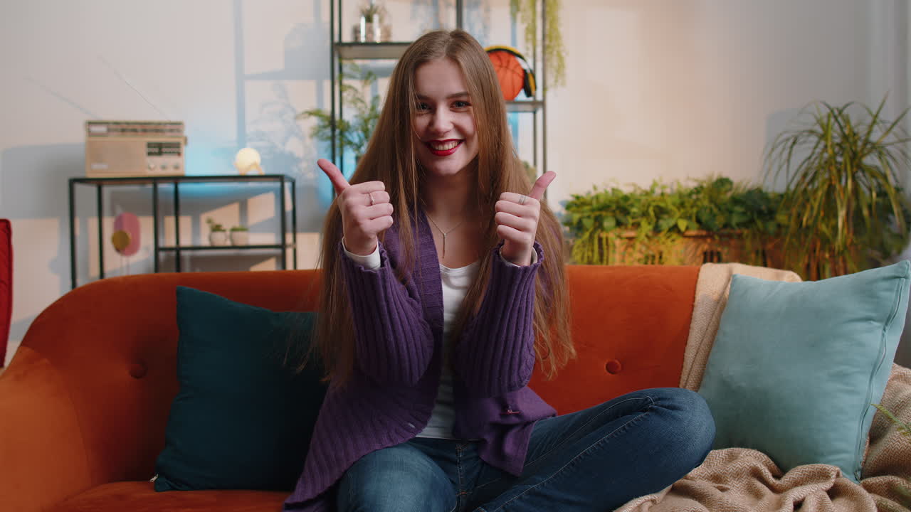 Happy young woman looking approvingly at camera showing thumbs up like positive sign good news