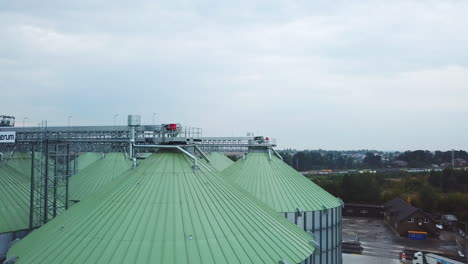 rising along a huge silver metal granary tank standing at the territory of modern silo plant. look at the slope roofs of elevators at the backdrop of farmlands.