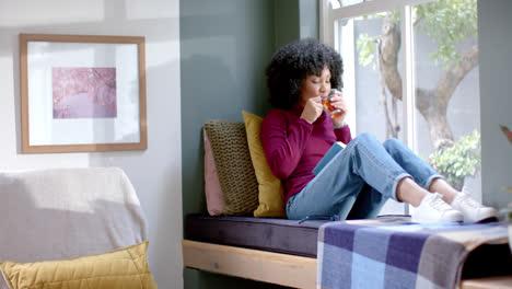 Biracial-woman-drinking-tea-and-reading-book-at-home,-slow-motion