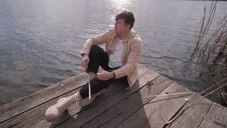 young man lies alone on wooden footbridge and staring at lake. thinking about life. peaceful atmosphere in nature. enjoying fresh air. back view.