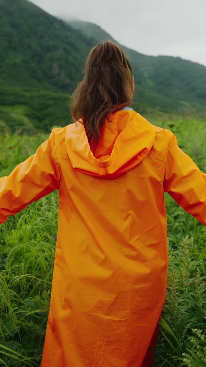 Woman in Orange Raincoat Standing in Green Mountain Landscape