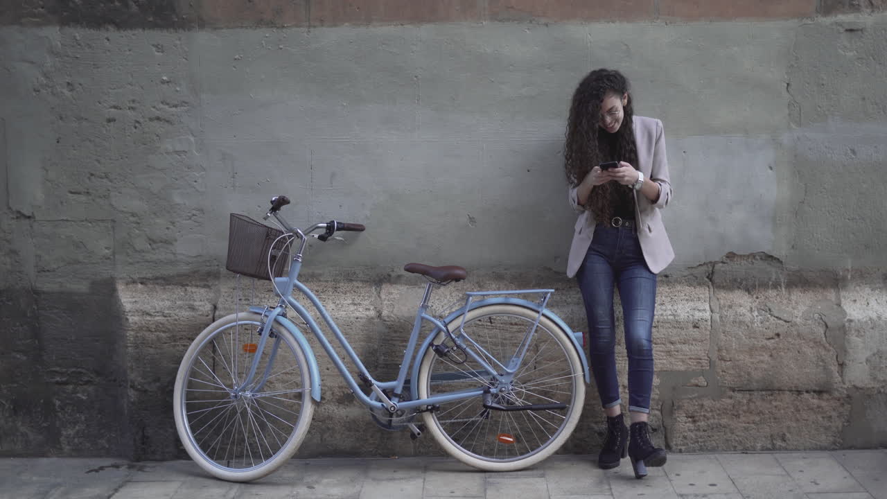 Woman with Curly Hair using Smartphone next to a Vintage Bicycle
