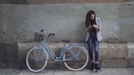woman with curly hair using smartphone next to a vintage bicycle