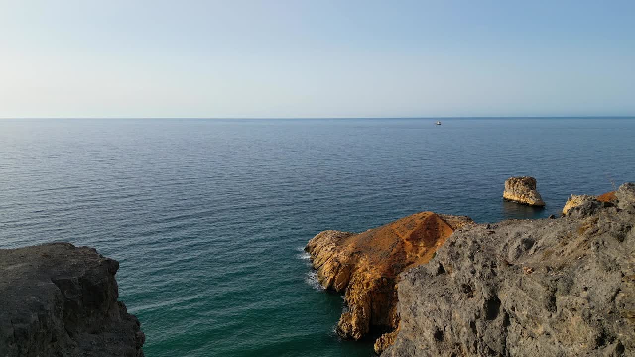 una vista aérea panorámica capta un majestuoso acantilado, una escarpada playa rocosa y un barco de carga lejano en el horizonte