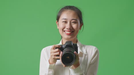 녹색 스크린에서 미소 짓는 카메라를 들고 있는 여자