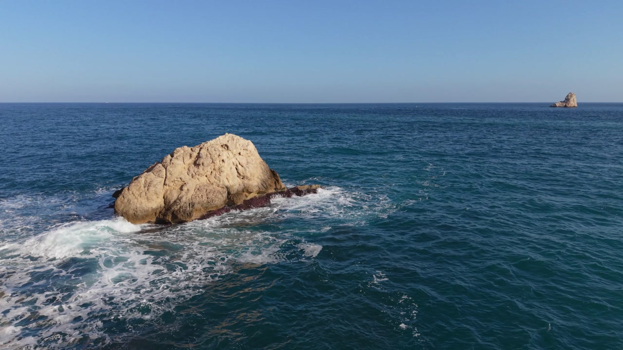 L’Estartit Costa Brava Spain Low slow flight at the foot of steep cliffs over rocks with clear blue sea lapping at their base in golden sun with clear blue sky