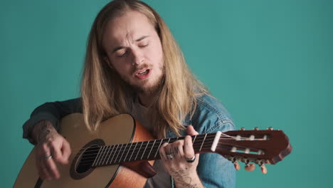 caucasian young man playing guitar and singing on camera.