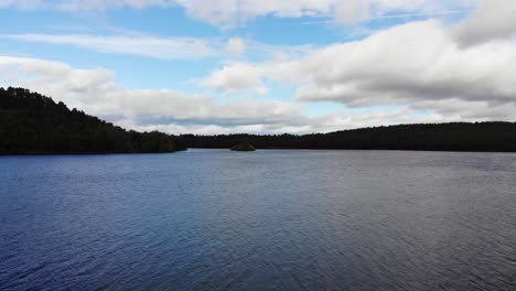 Vuelo-Aéreo-Sobre-La-Superficie-Del-Lago-An-Eilein-Rodeado-De-Pinos-Del-Bosque-De-Rothiemurchus