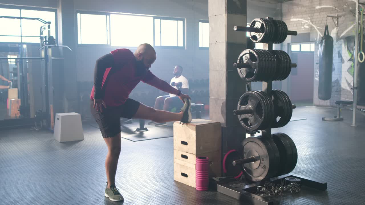 African American man starting with foot on plyo box, performing hamstring stretch in gym warming up