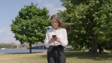 Classy-brunette-checking-smartphone-on-windy-sunny-day,-front-view