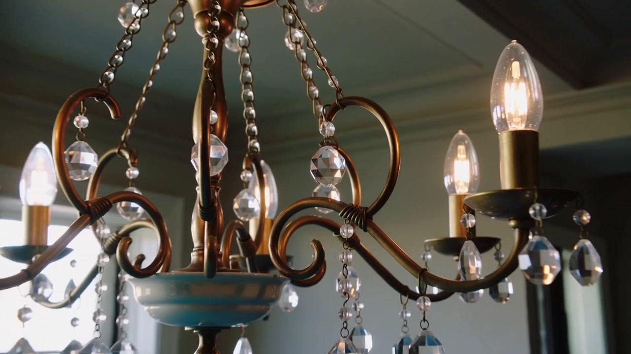Lampadario in ottone scintillante che mostra prismi mentre la telecamera si allontana nell'atrio, con lampadine accese.