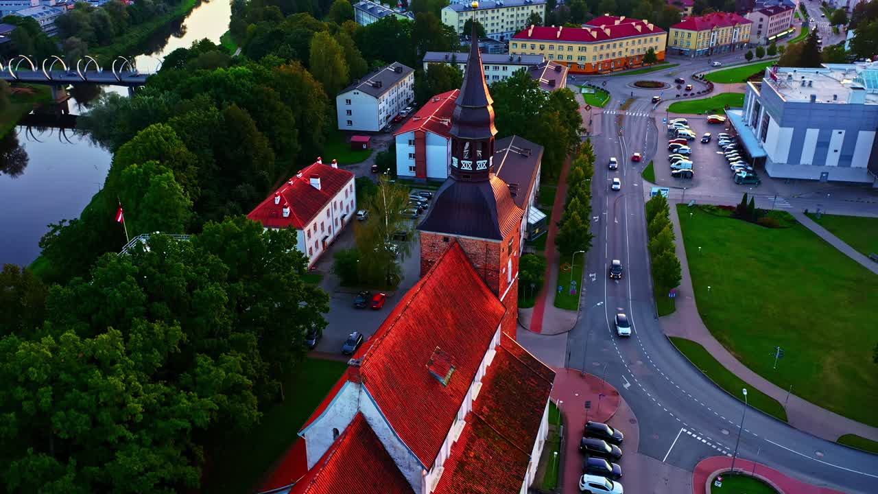 Panorama urbana di Valmiera con edifici, alberi verdi, fiume Gauja e un ponte moderno
