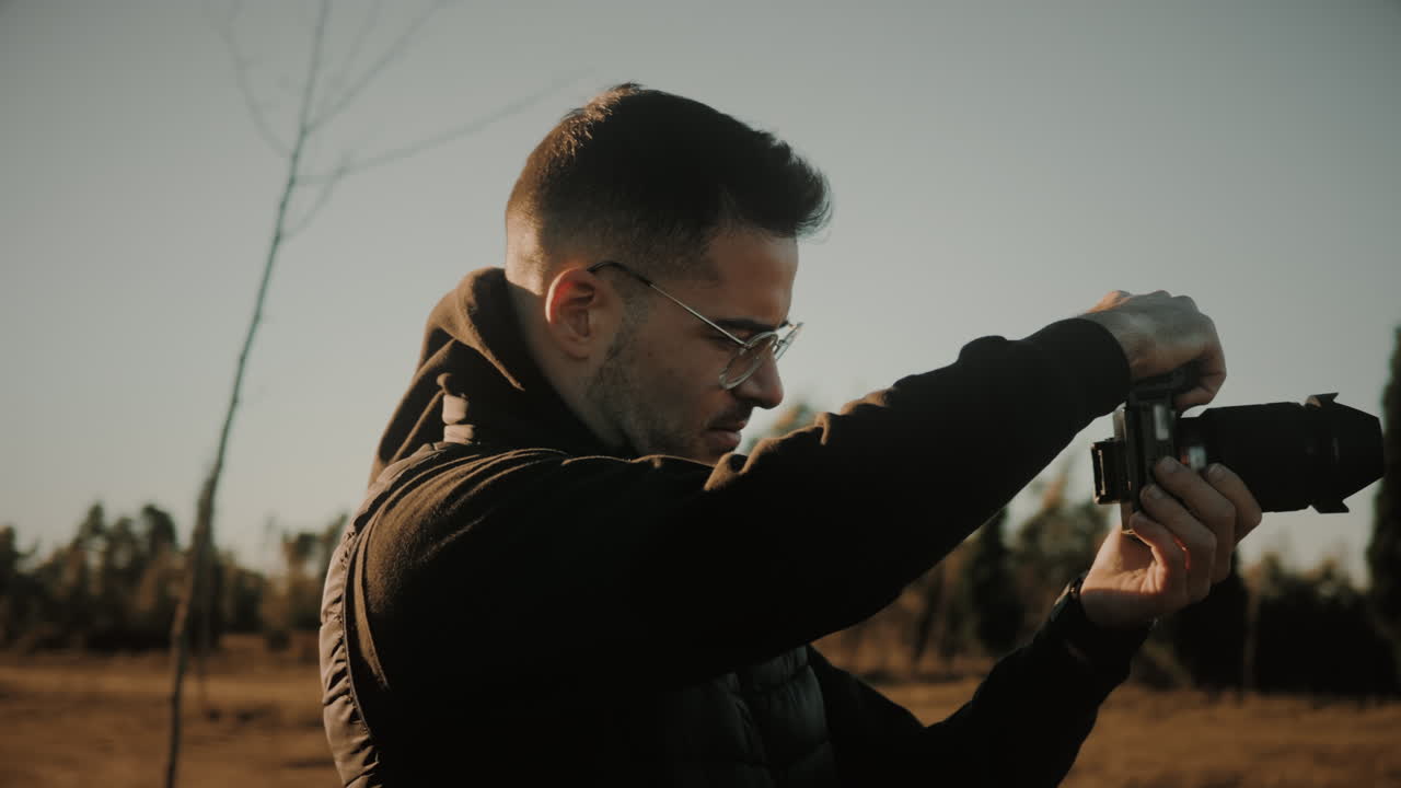 un fotógrafo masculino inspirador levanta su cámara dslr y toma una foto en la naturaleza al atardecer con el sol detrás de él creando una luz en el borde